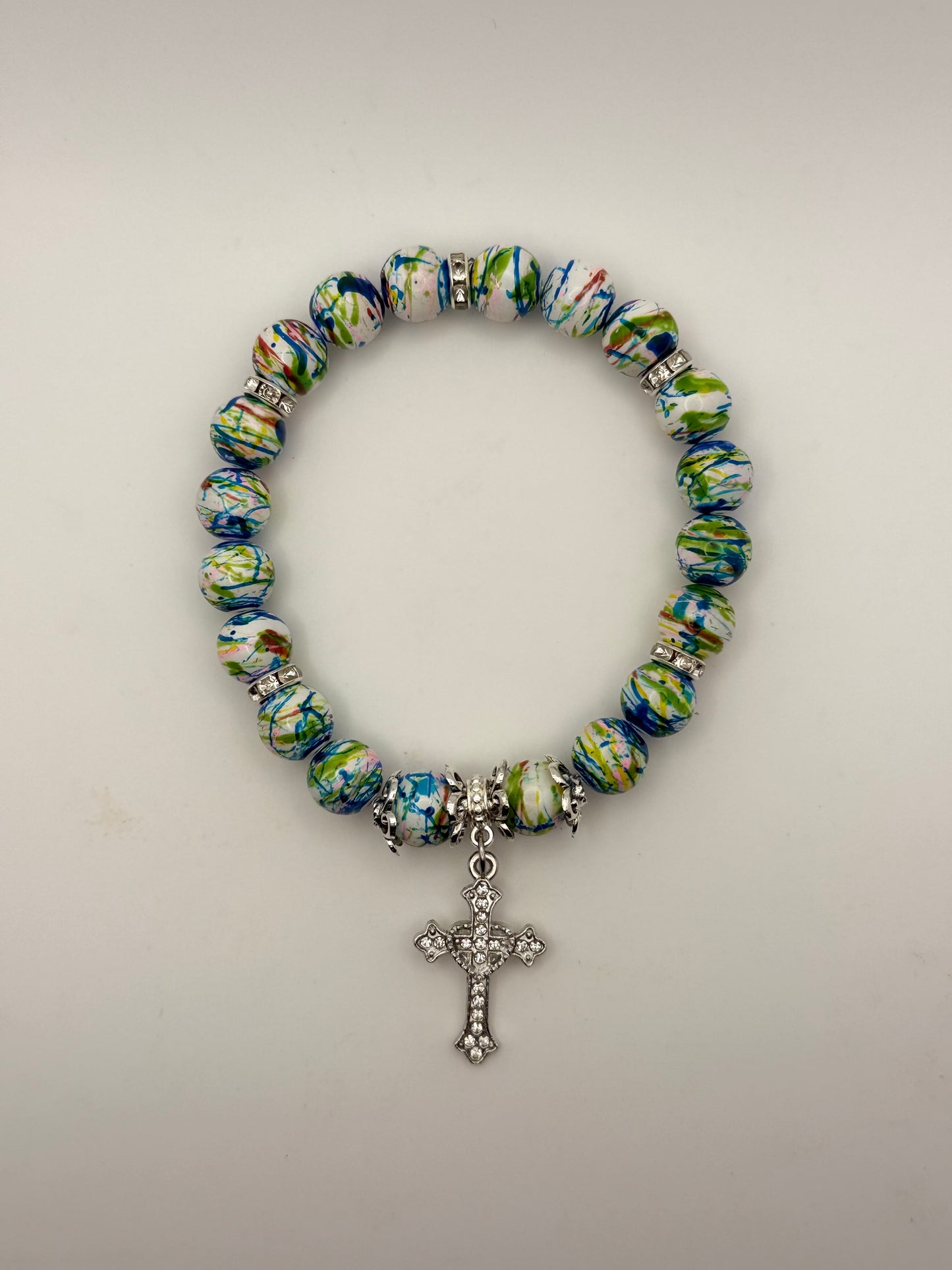 Multicolored beaded bracelet with a silver cross charm on a light gray background