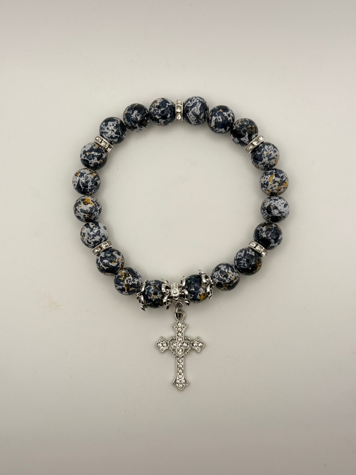 Bracelet with black and white marbled beads and a cross charm on a light gray background