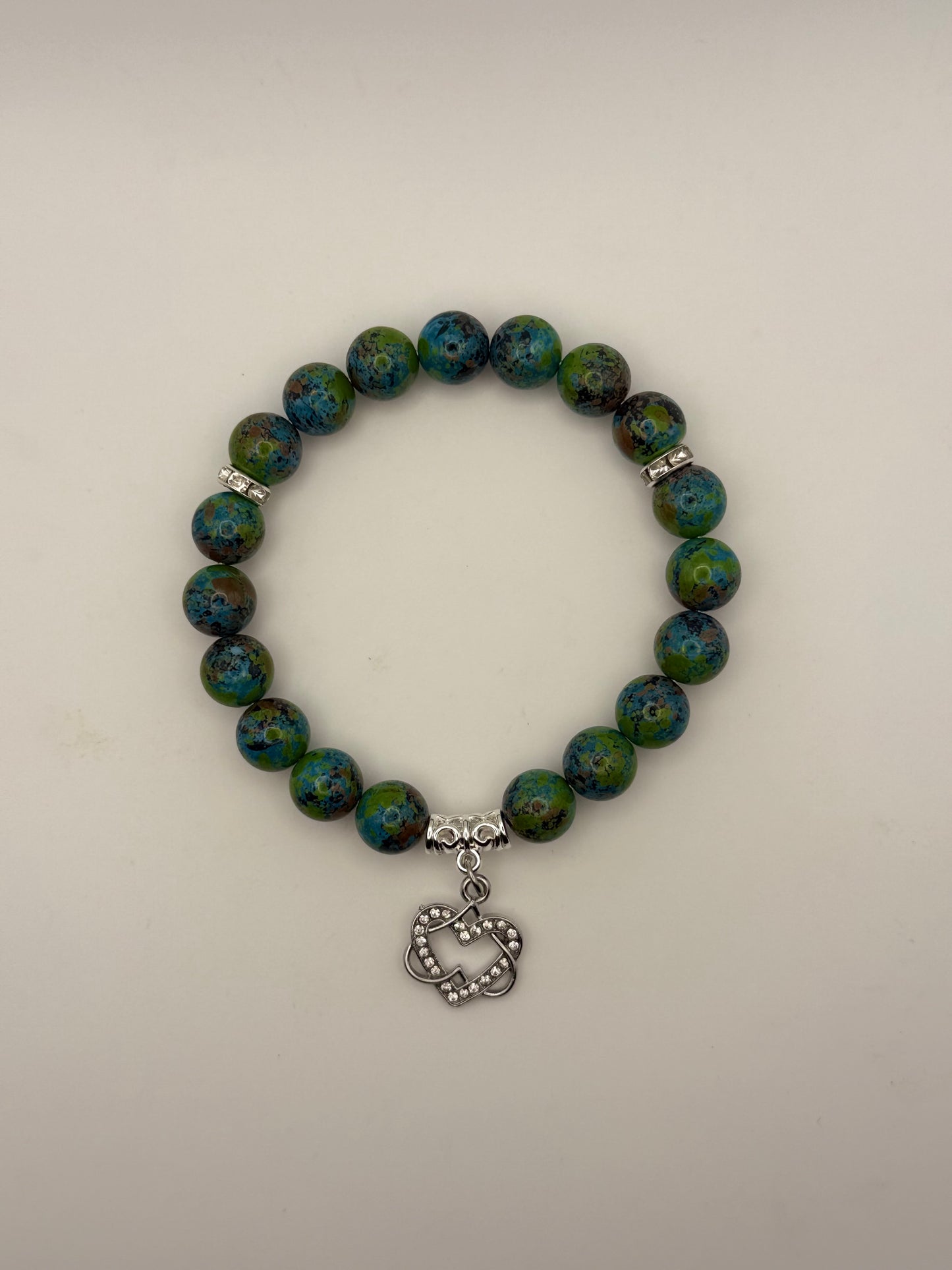 Bracelet with blue and green beads and a silver charm on a light gray background