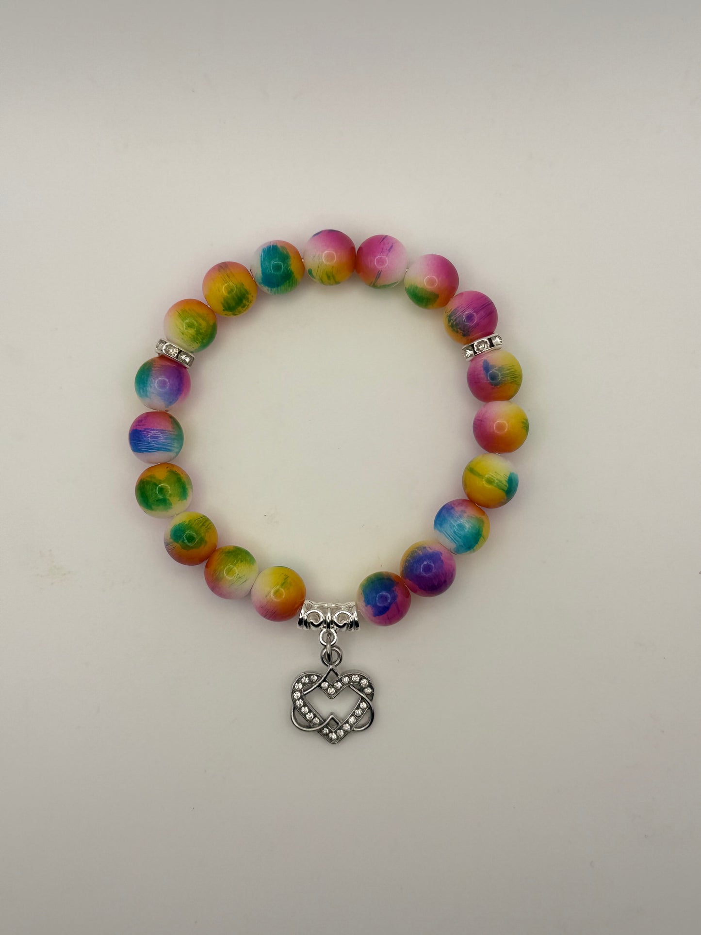 Multicolored beaded bracelet with a silver heart charm on a light gray background