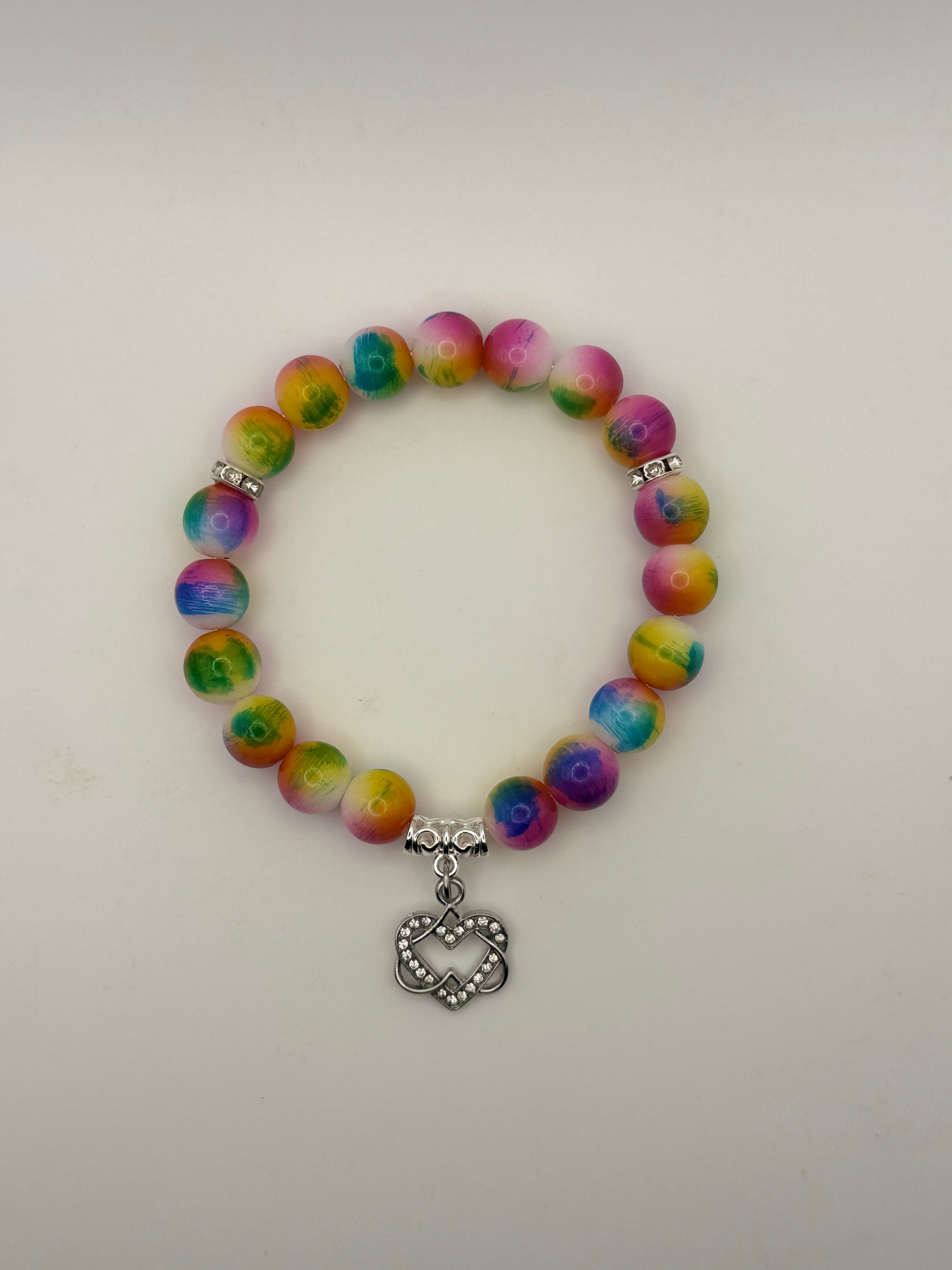Multicolored beaded bracelet with a silver heart charm on a light gray background