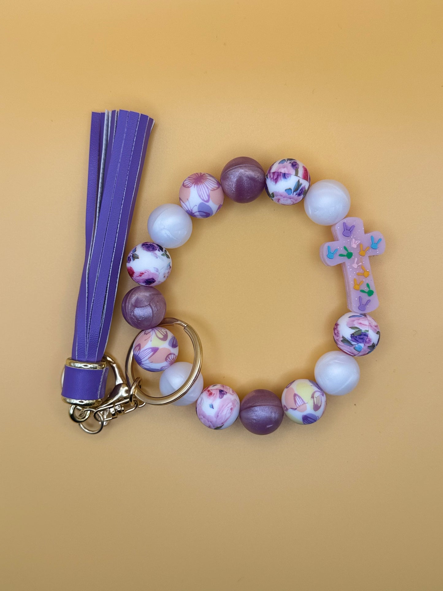 Beaded bracelet with floral designs and a purple strap on a beige background