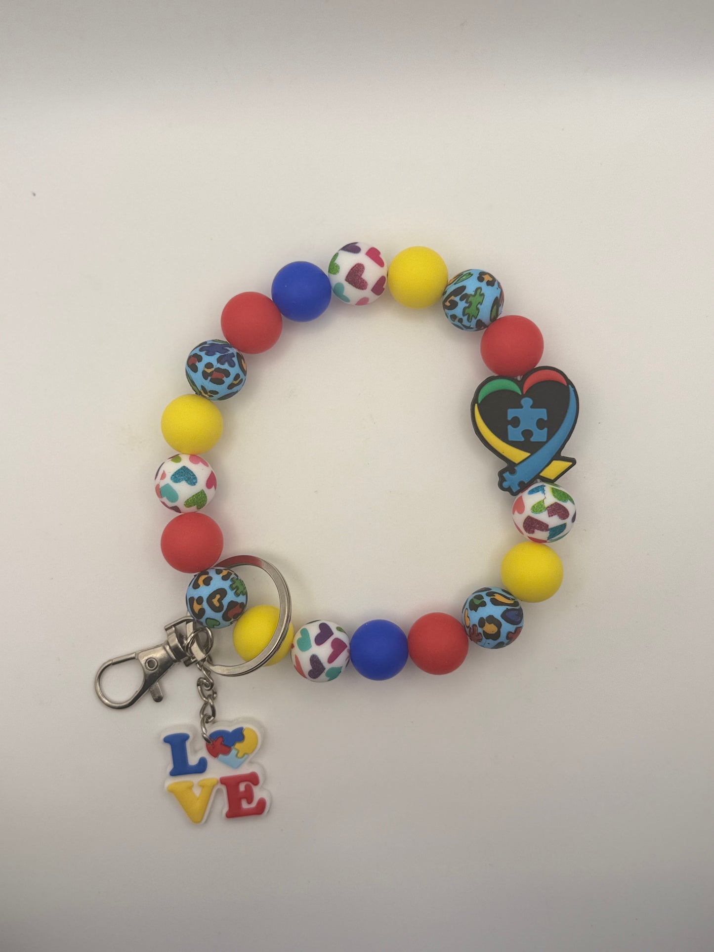 Colorful beaded bracelet with a keychain featuring a heart and puzzle piece design on a white background.