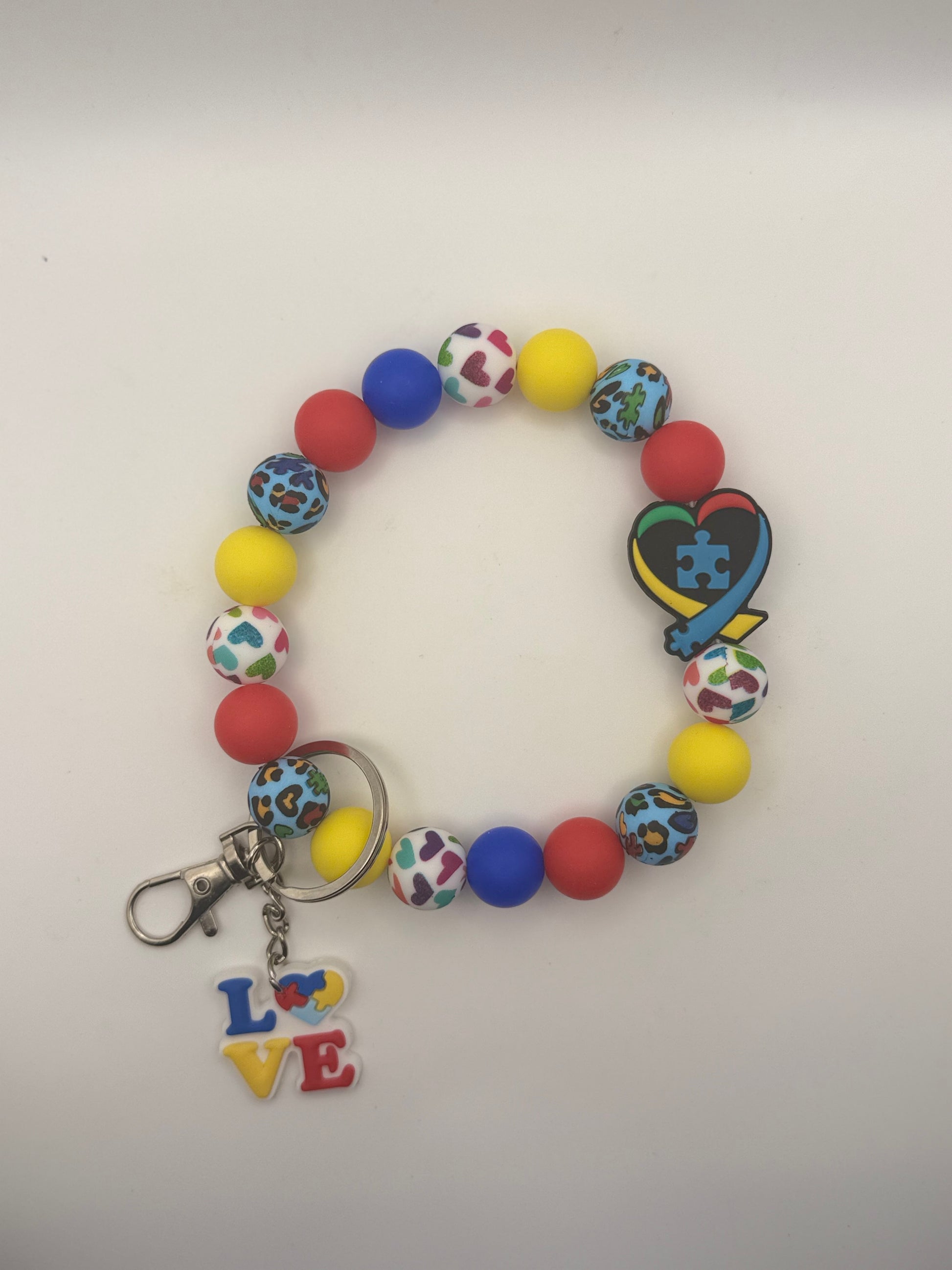 Colorful beaded bracelet with a keychain featuring a heart and puzzle piece design on a white background.