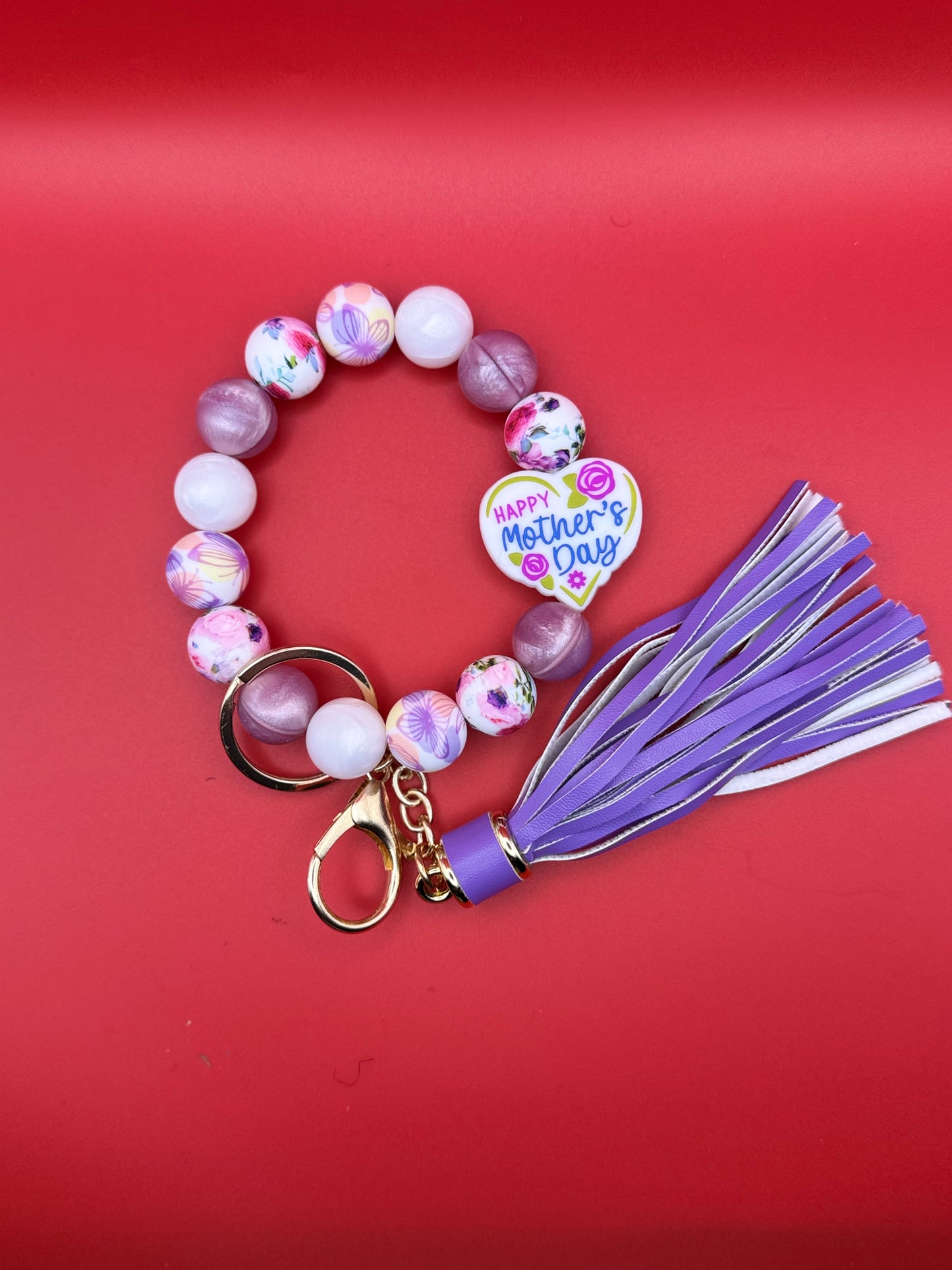 Beaded bracelet with a purple tassel and 'Happy Mother's Day' charm on a red background